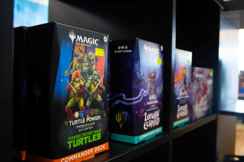 Shelf display of newest magic the gathering commander decks. Prominently, teenage mutant ninja turtle x mtg and lorwyn eclipsed mtg.